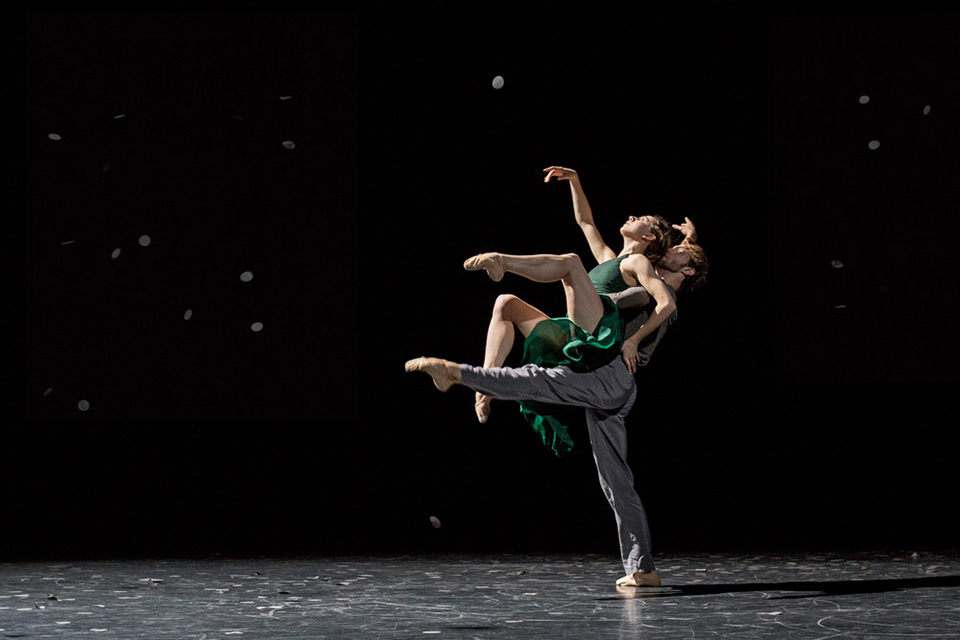 A man and a woman dancing together. The man is on one foot holding the woman up in the air, they are both looking up.