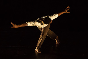 A man bent over with legs crossed and arms spread apart.