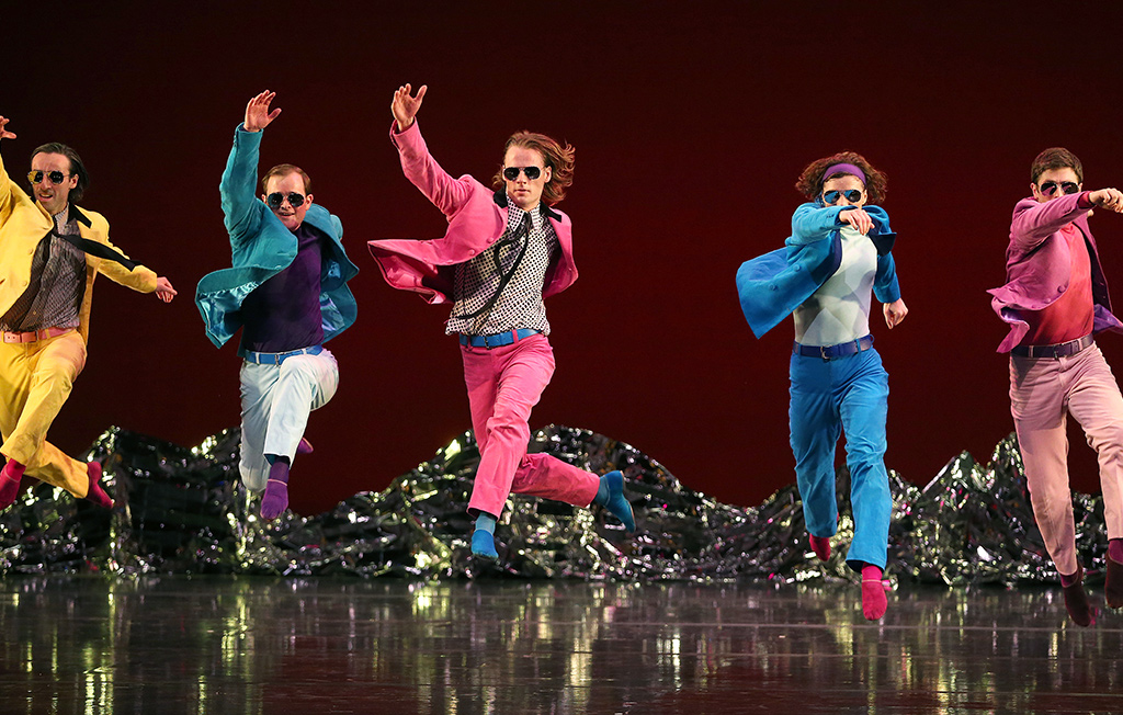 Five men in bright colorful suits and sunglasses jumping in the air.