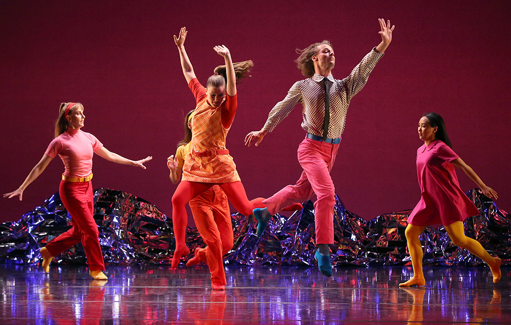 Five people in bright colorful clothing frolicking in various poses.