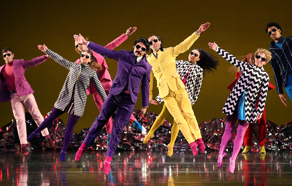 Men and women in sunglasses and bright colorful clothing jumping in the air with one arm sticking out.