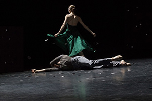 A woman in a green dress with back turned walking away from somebody lying on the ground.