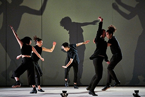 Five people in dressed in black with their large shadows cast behind them.